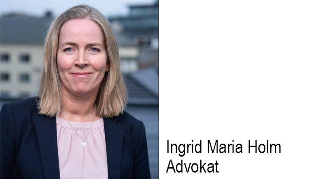 En kvinne med blondt hår og blazer smiler mot kameraet, med bygninger i bakgrunnen.