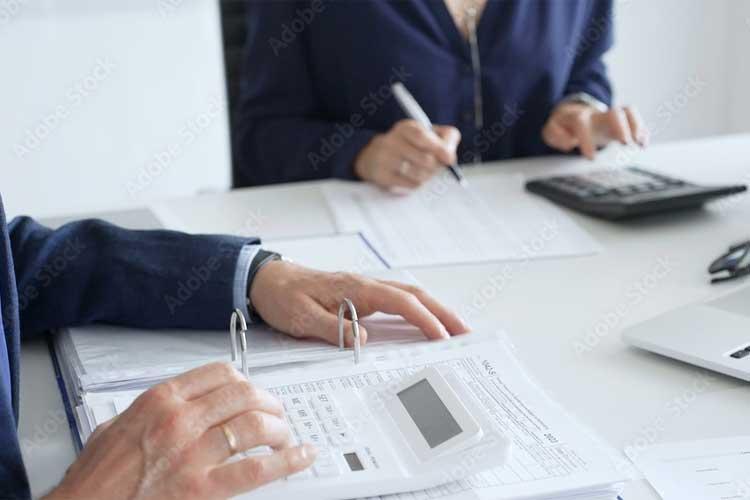 To personer som jobber med dokumenter og en kalkulator på et skrivebord. En av dem skriver med penn.