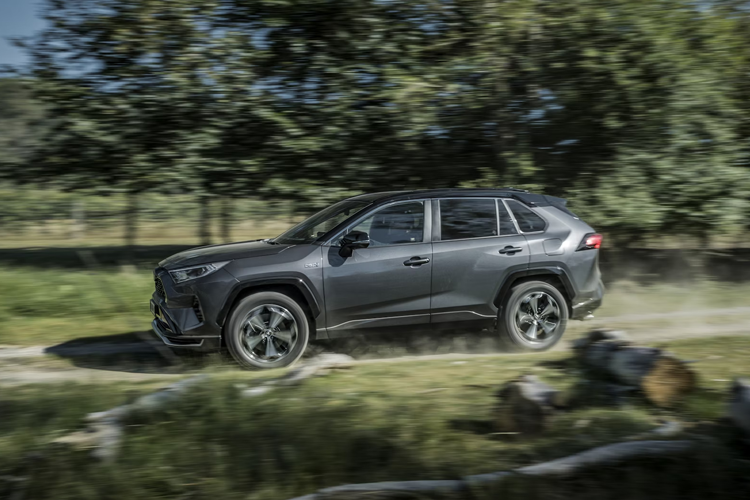 En grå SUV kjører raskt på en grusvei omringet av trær og natur.
