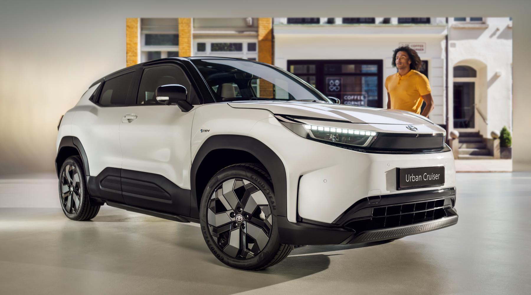 En moderne, hvit SUV med skarpe linjer står foran en bygning, med en kvinne i bakgrunnen.