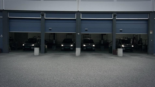Tre biler står parkert foran åpne garasjeporter i en moderne garasje.