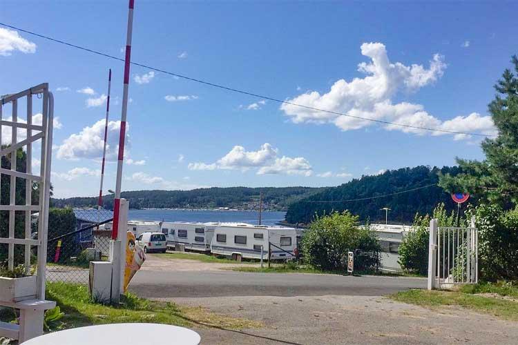 Utsikt over en campingplass ved sjøen med bobiler og grønt landskap under en blå himmel.