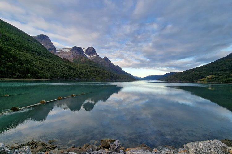 En vakker innsjø med fjell i bakgrunnen, speilbilde av landskapet i vannet under en skyet himmel.