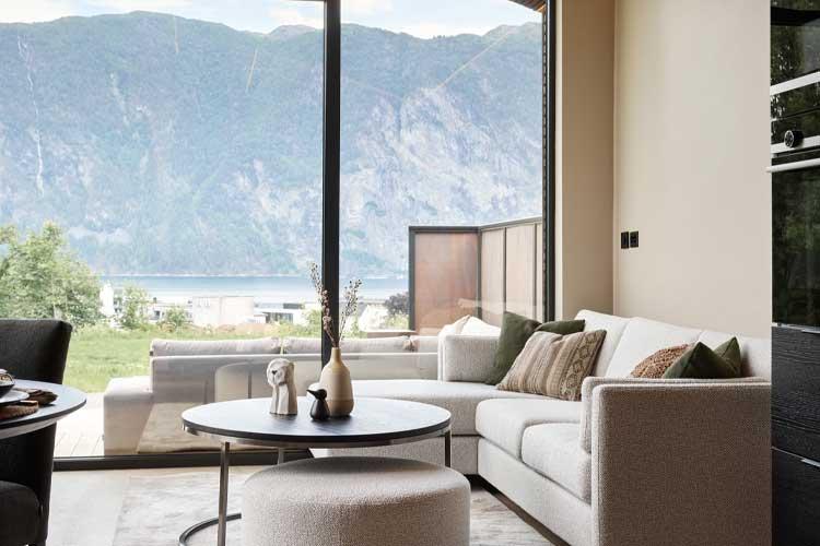 Moderne stue med hvit sofa, runde bord og store vinduer som viser fjellutsikt.