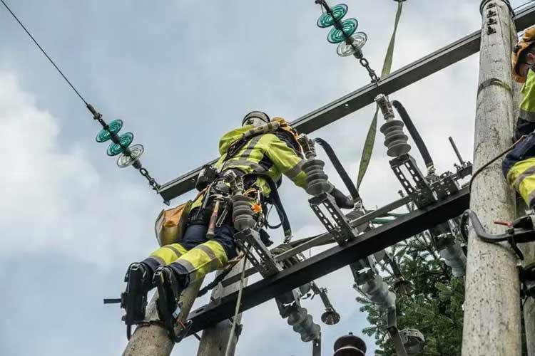 En linjearbeider klatrer opp en stolpe med elektrisk utstyr under en klar himmel.
