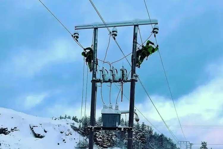 To personer som arbeider med strømledninger på en høyspentmast i snødekt landskap.