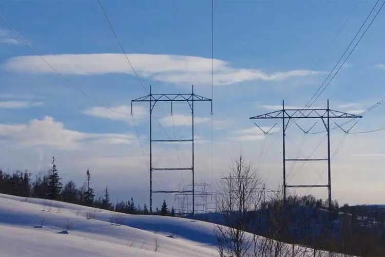 Høye kraftlinjer strekker seg over en snødekt bakgrunn med blå himmel og skyer.