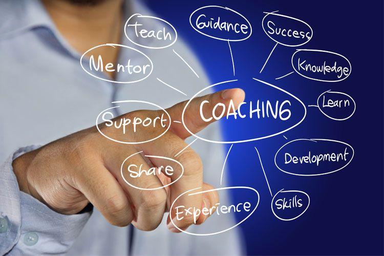 En person peker på en tavle med ord relatert til coaching, som veiledning, suksess og utvikling.