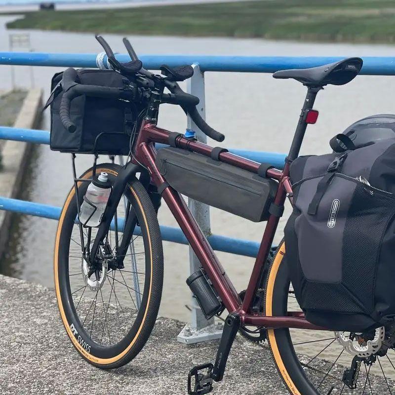 En rød sykkel med bagasje står på en brygge ved vannet, med en blå rekkverk i bakgrunnen.