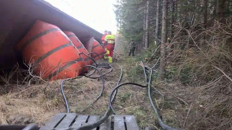Rødt og svart avfallstøtte som ligger på bakken, med redningspersonell i skogsområde. Kabelsystemer er synlige.