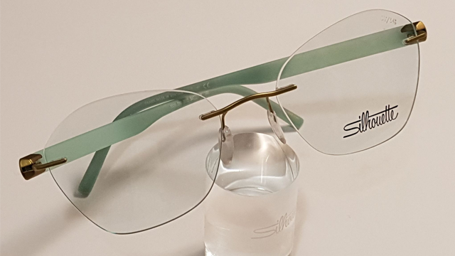 Et par stilige briller med grønne stenger og klart glass, plassert på en glassholder.