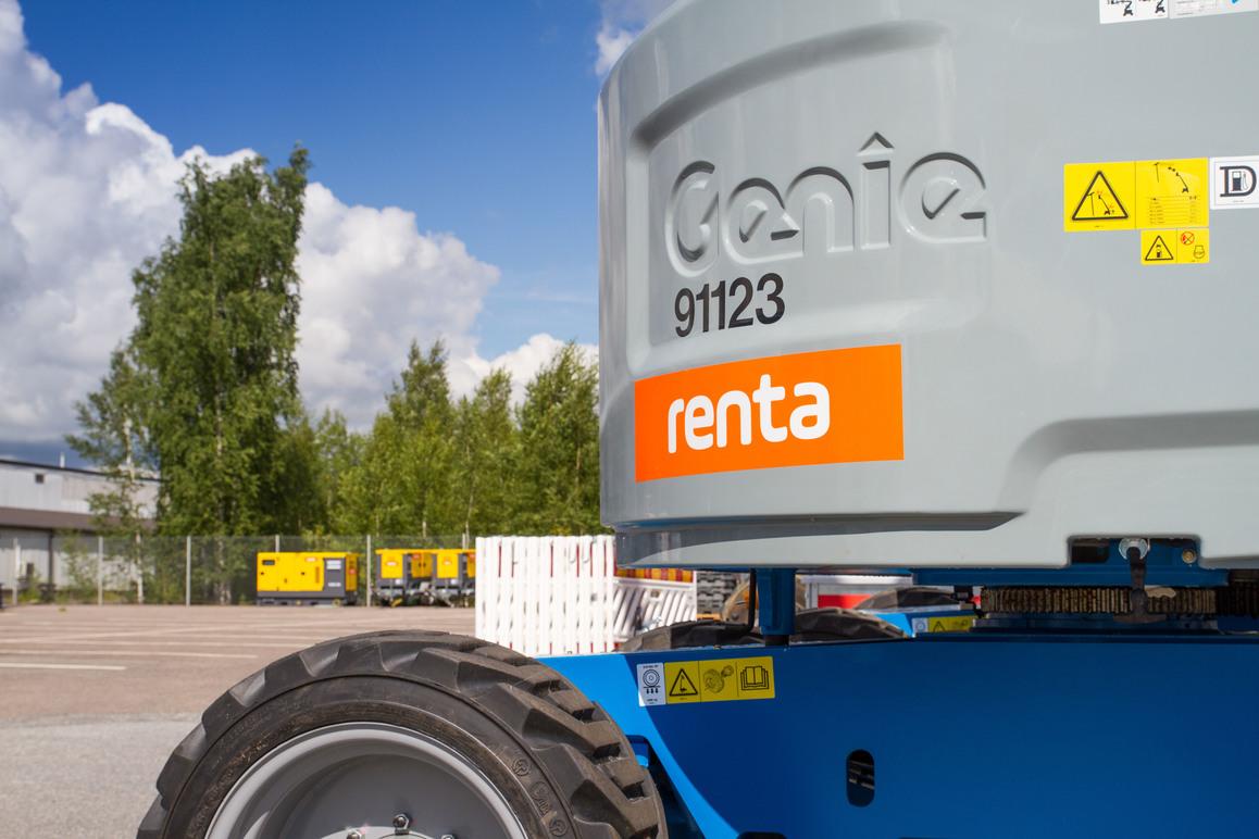 En Genie heis med Renta-logo, stående på en parkeringsplass med trær og bygninger i bakgrunnen.
