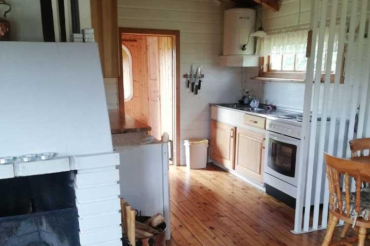 Kjøkken i en hytte med hvite skap, komfyr, peis og treverk på gulvet. Lys og koselig atmosfære.