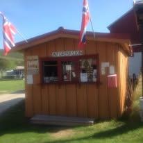 En koselig, rød og gul hytte med norske flagg, som fungerer som informasjonssenter i et naturskjønt område.