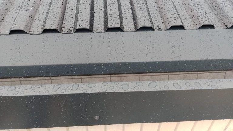 Vanndråper på et tak med metallplater, med en grå overflate og synlige dråper etter regn.
