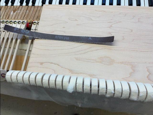 Bilde av en piano mekanisme med en treplate og en sandpapirstripe på en arbeidsbenk.