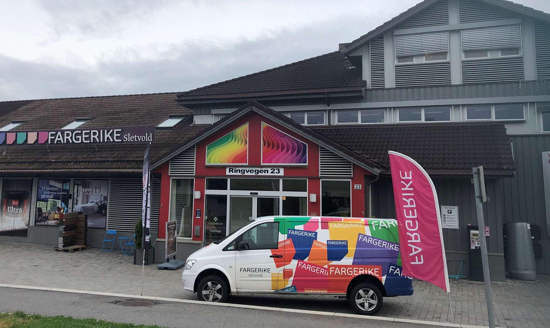 Fargerike butikk med fargerik bil parkert foran og flagg som viser butikkens navn.
