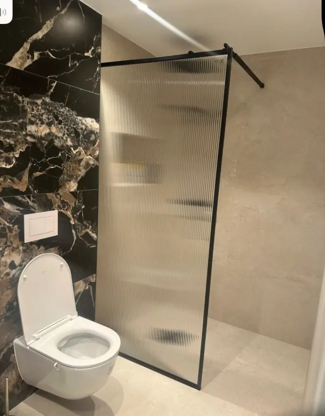 Moderne bad med dusjvegg i glass og toalett, dekorert med mørke marmorplater.