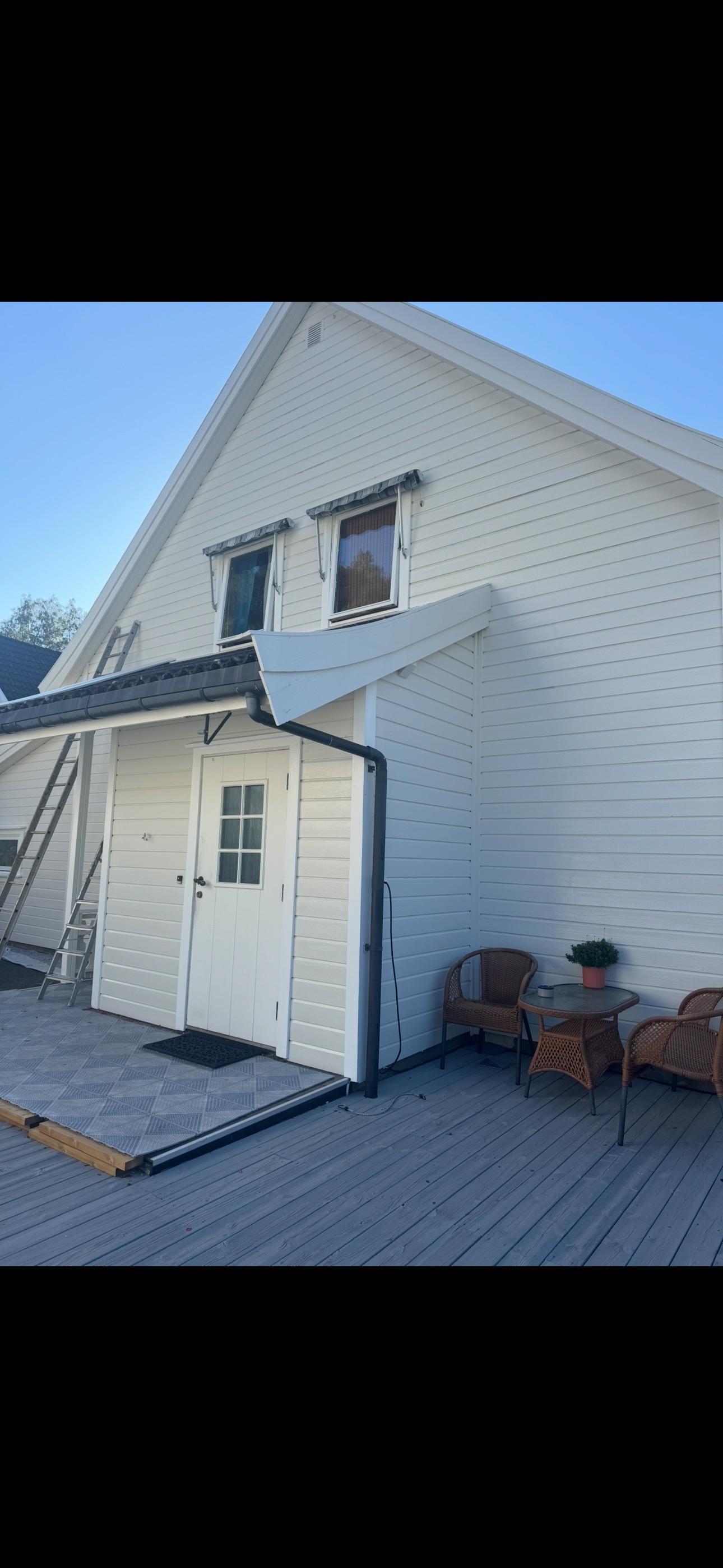 Hvit enebolig med terrasse og utemøbler, plassert i solfylt område.