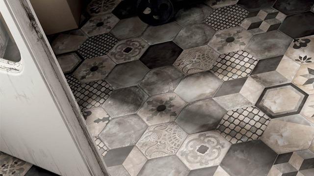 Gulv med hexagonale fliser i gråtoner og mønstre, sett fra en døråpning.