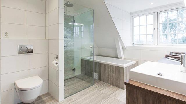 Moderne bad med dusj, badekar, toalett og vask med treverk og fliser i lyse farger.