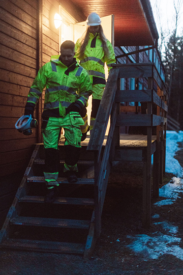 To personer i refleksjakker går ned trappen fra en hytte i skumringen.