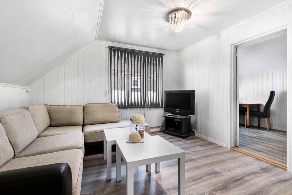 Lyst stue med sofa, hvite bord, TV og vindu med gardiner i en moderne hytte.