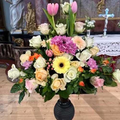 En fargerik blomsterbukett med roser, tulipaner, gerbera og prydplanter i en svart vase.