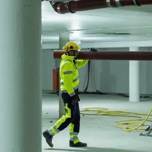 En arbeidstaker i verneutstyr går gjennom en underjordisk bygning med rør og elektriske ledninger.