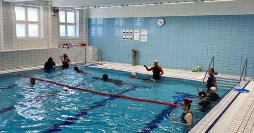 Svømmeundervisning i et svømmebasseng med flere personer som trener og en instruktør som gir veiledning.