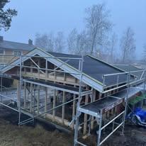 Byggetak med stillas under konstruksjon i tåke, med trevegger og takplater synlige.