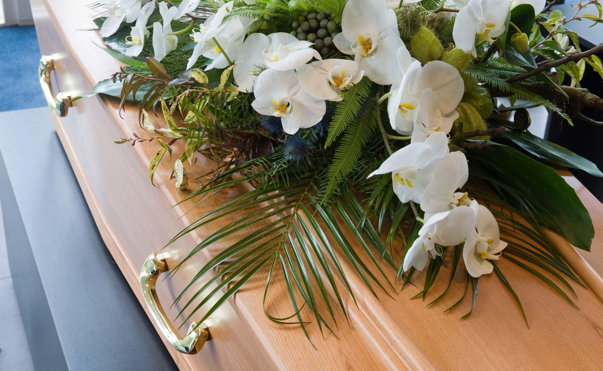 En kiste med hvite orkideer og grønt dekorasjon, plassert i et rom med blått teppe.