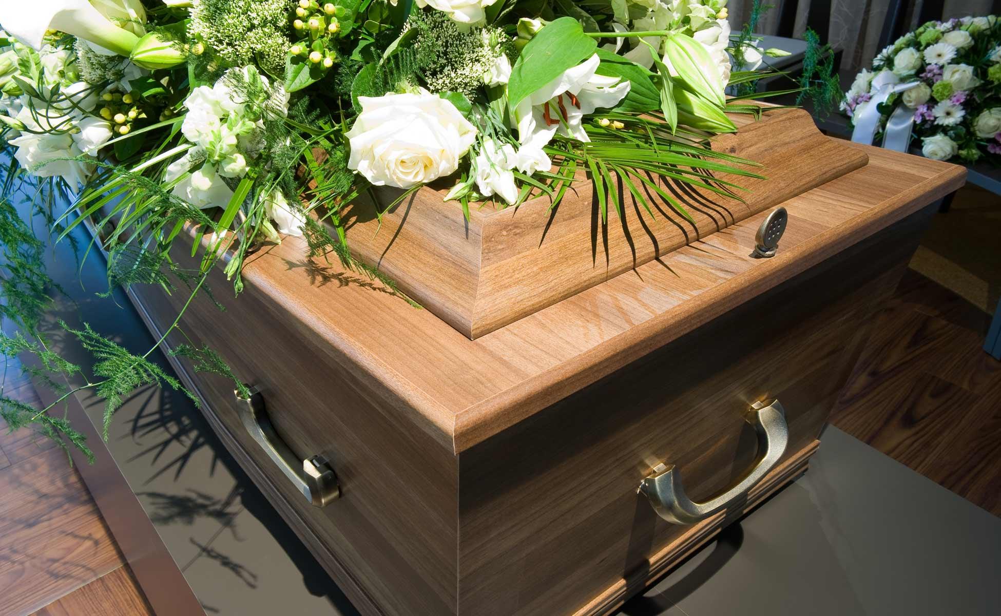 En kiste i tre med blomsteroppsats av hvite roser og grønt, plassert på en mørk overflate.
