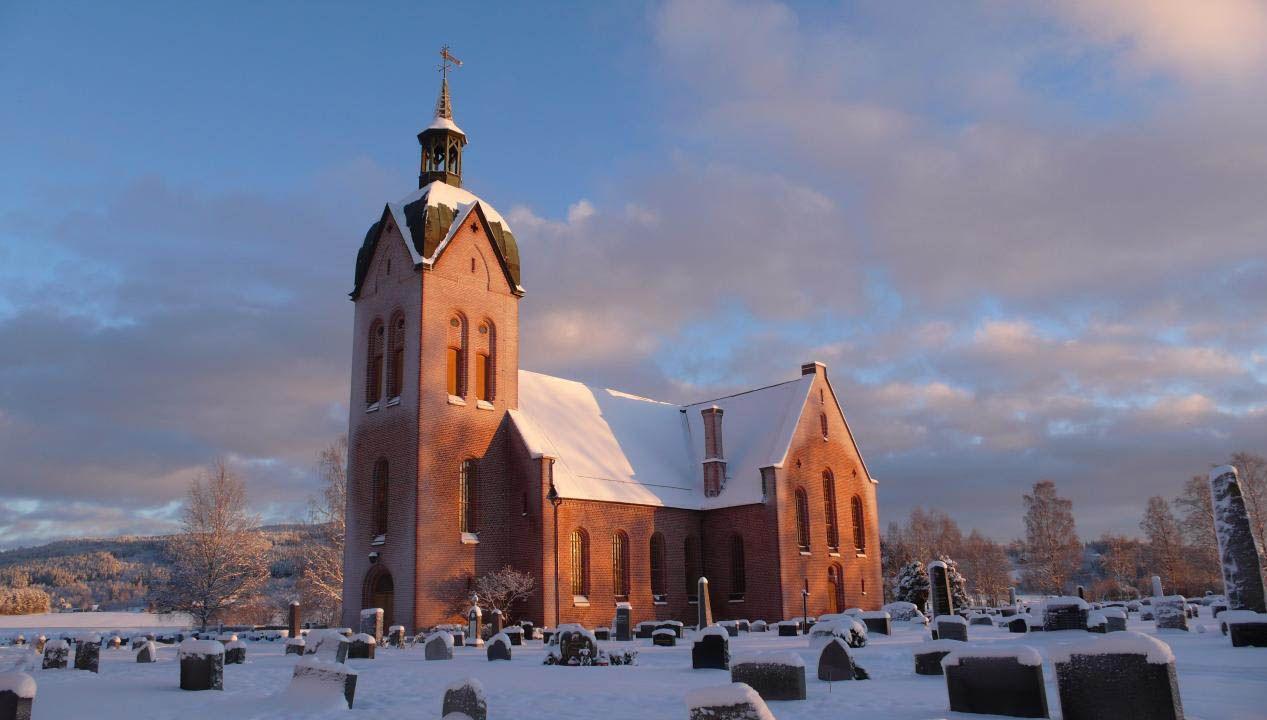 En vakker kirke dekket av snø, med en klokketårn og gravsteiner i forgrunnen under en blå himmel.