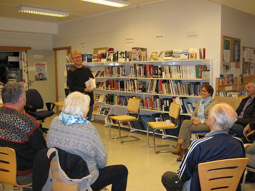 En gruppe mennesker sitter i et rom med bøker, mens en person står og holder en presentasjon.