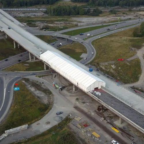 Luftbilde av en stor, hvit bygning som ligger over en motorvei med biler som kjører forbi.