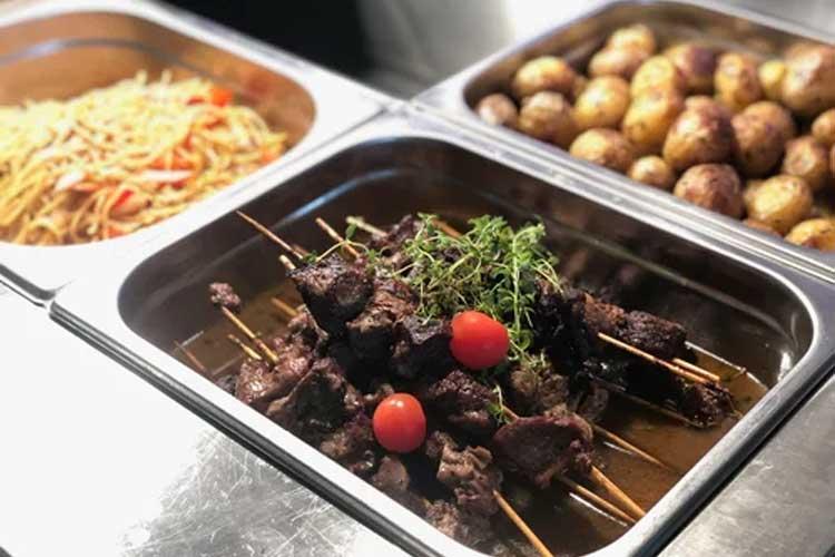Tre serveringsfat med mat: nudler med grønnsaker, poteter og grillspyd med kjøtt og cherrytomater.