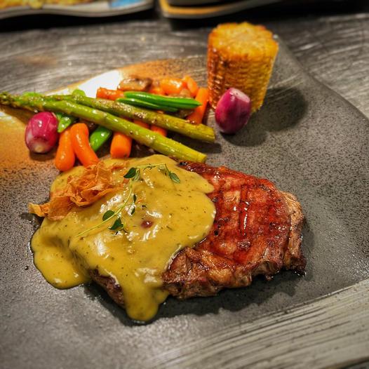 Saftig biff med kremet saus, servert med grønnsaker som asparges, gulrøtter og mais på en elegant tallerken.