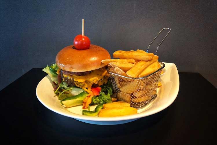 En saftig hamburger med ost, salat og tomat, servert med sprø pommes frites i en kurv.