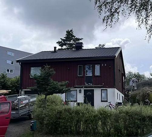 Rødt hus med svart tak, omgitt av busker og trær, med en sykkel parkert foran inngangen.