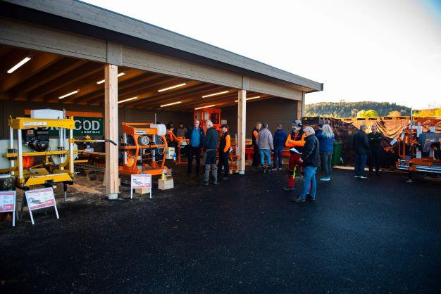 Mennesker samles utenfor en bygning med landbruksmaskiner og utstyr under en messe eller arrangement.