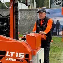 En mann i oransje og svart arbeidsklær står ved en LT 15 maskin på en utstilling.