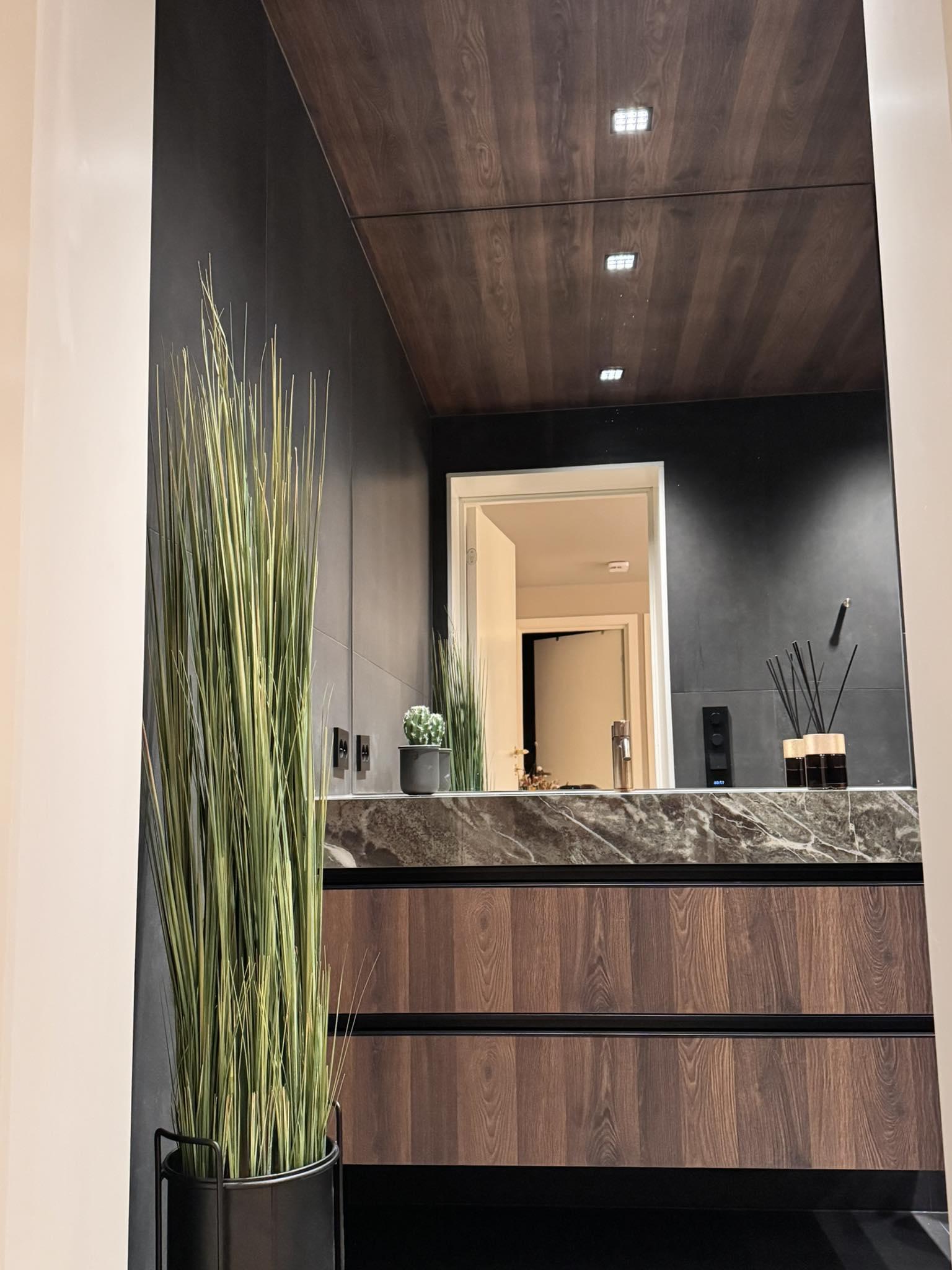 Moderne bad med trepanel, marmorbenk og grønne planter i en stilren innredning.