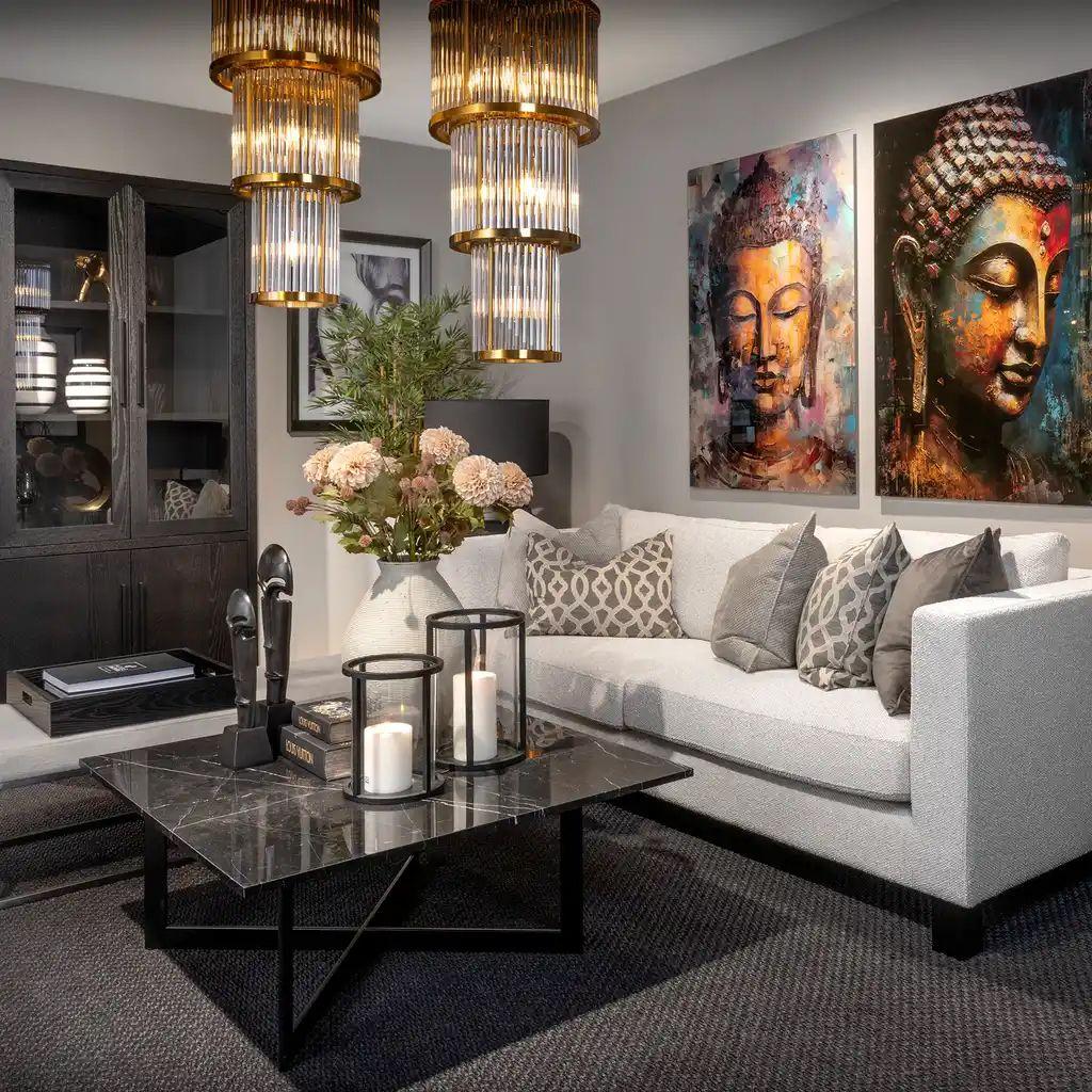 Moderne stue med grå sofa, kunstverk av Buddha, stilige lamper og et bord med lysestaker og blomster.