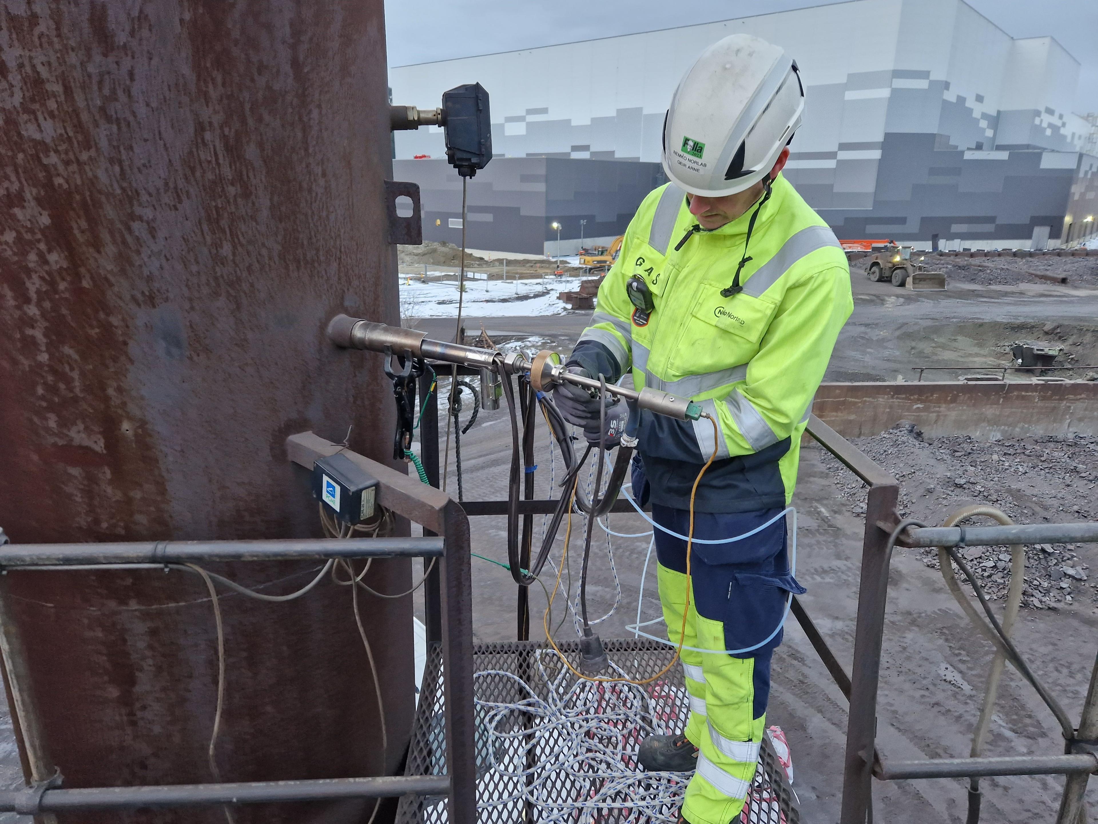 En arbeidstaker i verneutstyr kobler ledninger på en stålstolpe på en byggeplass.