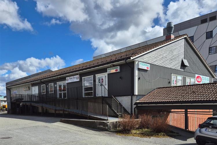 En grå bygning med flere vinduer og skilt, beliggende på en gate under en blå himmel med skyer.