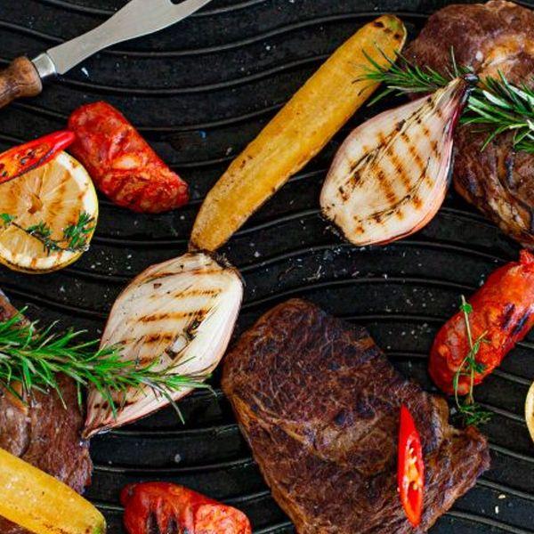 Grillet biff med poteter, løk, chorizo og sitron på en svart grillplate, dekorert med urter.