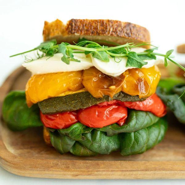 En fargerik sandwich med spinat, paprika, squash, mozzarella og brød, servert på en treplate.
