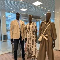 Tre mannequiner i en butikkvindu, iført en beige blazer, en blomstrete kjole og en grønn buksedress.