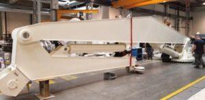 Stort hvitt maskindel i en fabrikk, med arbeidere som jobber i bakgrunnen.